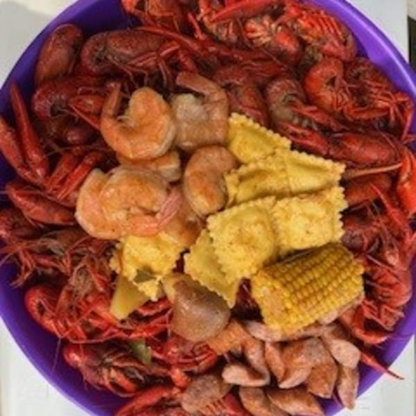 A purple bowl overflowing with Krawfish Kai's seafood boil, including crawfish, shrimp, corn, and ravioli.
