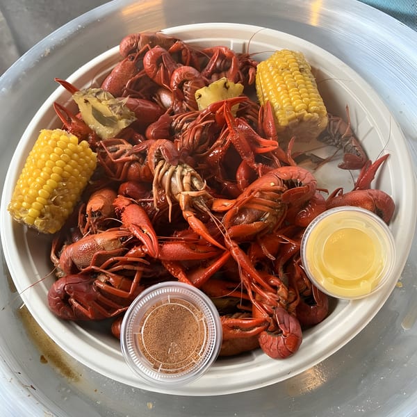 A white plate overflowing with Krawfish Kai's red crawfish, corn on the cob, pineapple, and dipping sauces.