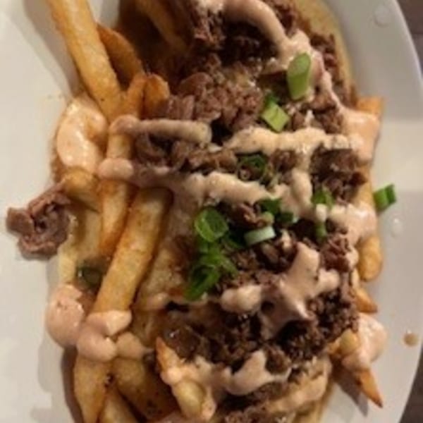 Krawfish Kai's fries topped with seasoned meat, creamy sauce, and green onions on a white plate.