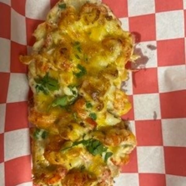 Krawfish Kai's cheesy crawfish bread, topped with green herbs, on red and white checkered paper.