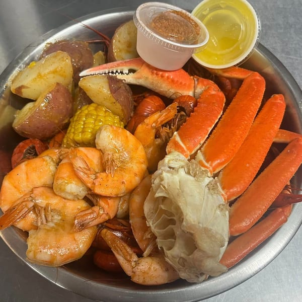 A Krawfish Kai seafood boil with crab legs, shrimp, crawfish, corn, and potatoes in a metal bowl.