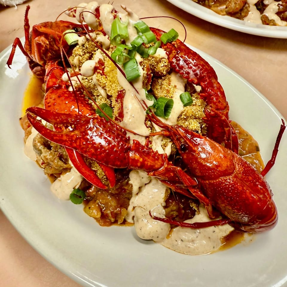 Boiled crawfish with creamy sauce, green onions, and crispy topping on a white plate.