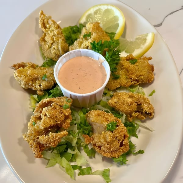 Fried oysters on a bed of lettuce with a side of dipping sauce and lemon wedges.