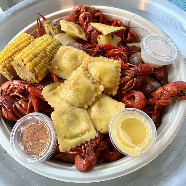 Boiled crawfish, corn on the cob, potatoes, and ravioli in a white bowl with dipping sauces.