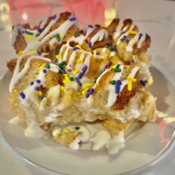 Bread pudding drizzled with white icing and Mardi Gras colored sprinkles on a white plate.