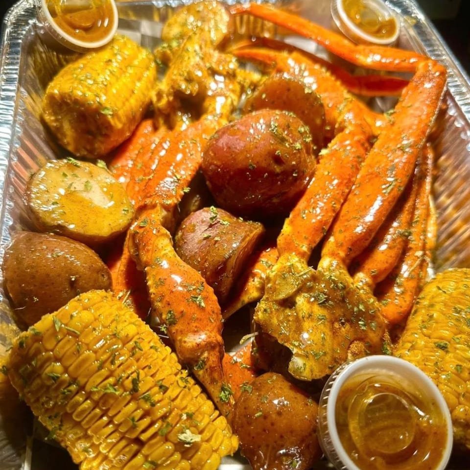 Krawfish Kai's seafood boil with crab legs, corn on the cob, and potatoes in a foil pan.